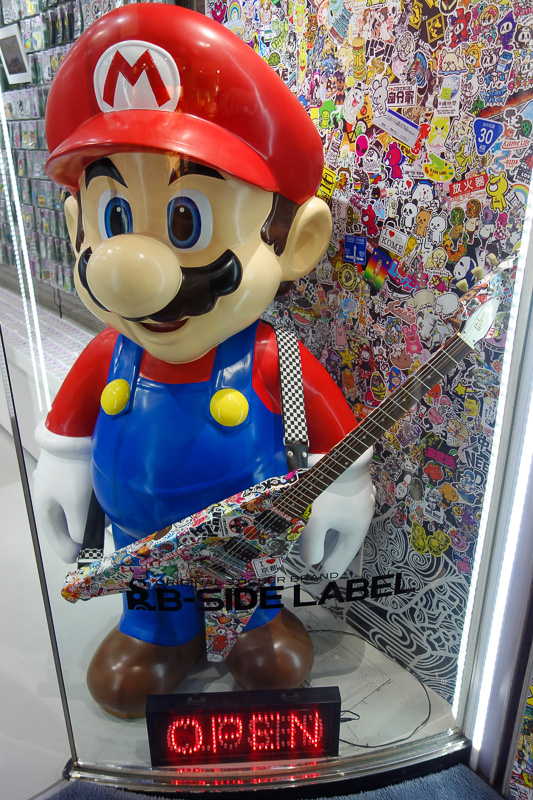 Hong Kong - Japan - Taiwan - March 2014 - Super mario is holding a genuine Gibson Flying V. This is just a trading card shop, which has nothing to do with Nintendo or $2500 guitars.