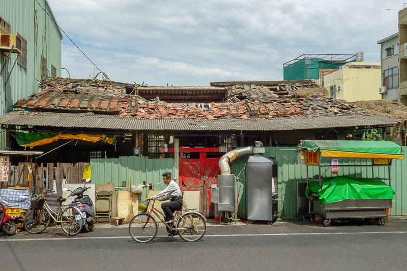 A full lap of Taiwan in March 2017 - Across the road from the temple, things are not so good. I call this sad old man cyclist pedals past collapsing roof. Prints available, various sizes.